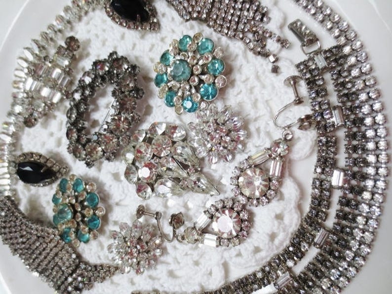 May include: A collection of vintage rhinestone jewelry pieces, including necklaces, earrings, and brooches. The jewelry is made of silver-toned metal and features clear and blue rhinestones.