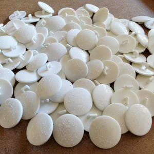 May include: A large collection of round white plastic buttons, each featuring a raised, intricate snowflake-like pattern on the front surface and a single loop shank on the back for attachment to fabric or other materials.