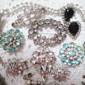 May include: A collection of vintage jewelry featuring a variety of styles, including crystal brooches, rhinestone necklaces, and a pair of black sunglasses.