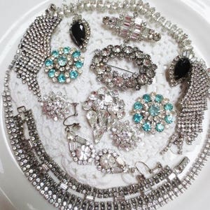May include: A collection of vintage rhinestone jewelry pieces, including necklaces, earrings, and brooches. The jewelry features clear and turquoise rhinestones, as well as black stones.