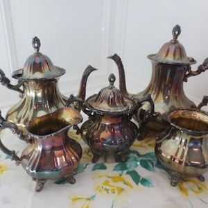 May include: A silver tea set with a teapot, creamer, sugar bowl, and a matching lidded serving dish. The set has a classic design with a fluted body and ornate handles.