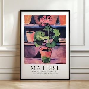 Può includere: Una stampa artistica incorniciata di "Vaso di Gerani, 1912" di Matisse. Il dipinto presenta un geranio rosa in un vaso di terracotta, con foglie verdi, sullo sfondo di altri vasi e una finestra. L'opera è esposta su sfondo bianco.