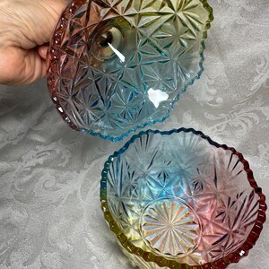 May include: Two iridescent glass bowls with a starburst pattern. The bowls have a scalloped edge and transition from red to yellow to blue. The bowls are likely for serving or display.