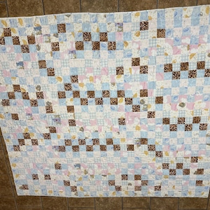 May include: A handmade quilt with a patchwork design. The quilt features a pattern of alternating squares in light blue, pink, and white, with brown leopard print squares. The quilt is likely made of cotton and is suitable for a bed or as a decorative throw.