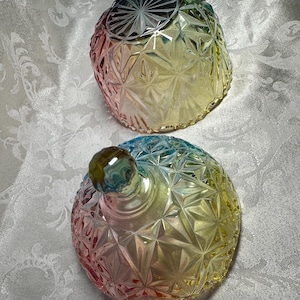 May include: Two decorative glass jars with lids. The jars are a rainbow of colors, including pink, yellow, and blue. The jars have a geometric starburst pattern. The lid of one jar is off, revealing the inside.