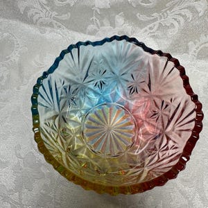 May include: A colorful, iridescent glass bowl with a starburst pattern. The bowl has a scalloped edge and transitions from yellow to red, blue, and green. The bowl is likely vintage and suitable for serving.