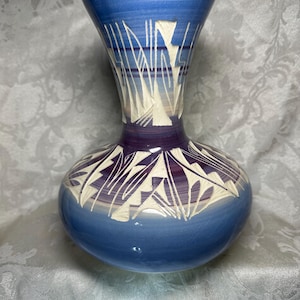 May include: A handcrafted ceramic vase with a bulbous base and a flared top. The vase features a gradient of blue hues, transitioning from a deep indigo at the base to a lighter sky blue at the top. White geometric patterns and lines adorn the surface.