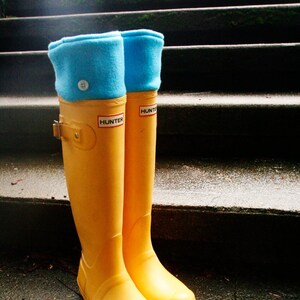 May include: A pair of yellow rubber rain boots with blue fleece cuffs. The boots have the word "HUNTER" printed on the side.