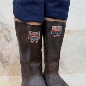 May include: A pair of brown Xtratuf neoprene boots with navy blue fleece cuffs. The boots have a red and white logo that says "XTRATUF" and "Made in USA". The boots are on a map.