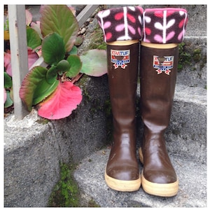 Puede incluir: Un par de botas de goma marrón con suelas blancas y polainas de lana de color rosa y blanco. Las botas están etiquetadas con "Xtratuf" y "neopreno" con un diseño de estrella rojo, blanco y azul.