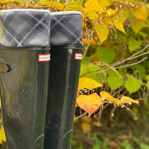 May include: A pair of black tall rain boots with grey and black plaid fleece boot cuffs. The boots have the word "HUNTER" printed on the side.