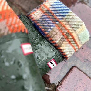 Puede incluir: Botas de lluvia de goma verde con forro de lana a cuadros. Las botas tienen una etiqueta blanca con la palabra "Hunter" en ellas.