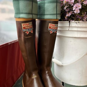 May include: A pair of brown rubber boots with green and white plaid fleece boot cuffs. The boots have a label that reads "XTRATU Neoprene Made in USA".