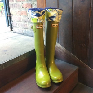 Puede incluir: Un par de botas de lluvia Hunter verdes con polainas de estampado floral. Las botas tienen el logotipo de Hunter en el lateral.