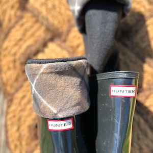 May include: A pair of black Hunter rain boots with plaid fleece boot cuffs. The boots have the Hunter logo on the side.