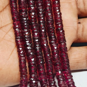 May include: Strands of faceted, deep red gemstone beads. The beads are small, flat, and disc-shaped, strung together to form multiple strands. The color is a rich, dark red, with a slight sparkle from the facets. The beads are held in a hand.