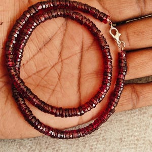Puede incluir: Un collar compuesto por pequeñas gemas facetadas de color rojo oscuro. Las cuentas están ensartadas, formando una doble hebra. Un cierre plateado asegura el collar. Las gemas tienen un color rojo oscuro intenso.