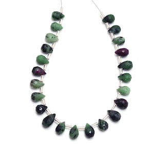 May include: Two strands of teardrop-shaped gemstones in green and deep red. The beads are strung on a thin, silver wire, with small silver tubes separating each gem. The gemstones have a faceted surface and vary in size.