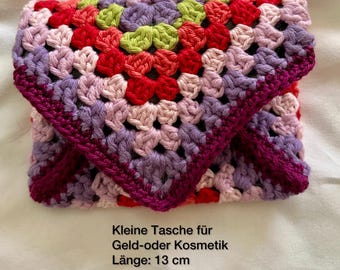 May include: Handmade crochet clutch in a granny square pattern. The clutch features a vibrant mix of red, pink, purple, and green. The dimensions are approximately 5.1 inches in length and 3.9 inches in height. The text on the image says "Handmade".