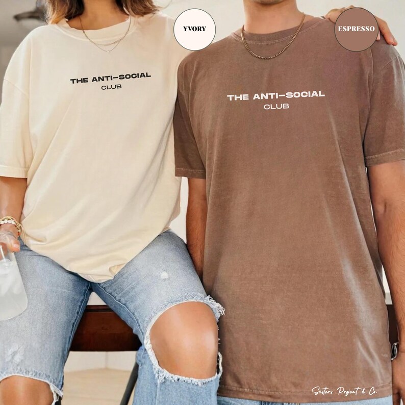 K&ouml;nnte beinhalten: Zwei kurz&auml;rmelige T-Shirts, eines in Elfenbein und eines in Espresso, jeweils mit dem Text "THE ANTI-SOCIAL CLUB" in Wei&szlig;. Das elfenbeinfarbene Shirt wird mit hellblauen Jeans kombiniert. Das Espresso-Shirt wird mit hellblauen Jeans kombiniert.