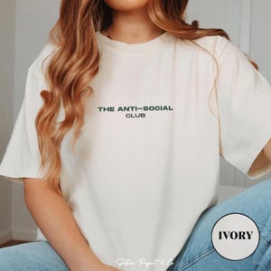 K&ouml;nnte beinhalten: Cremefarbenes T-Shirt mit dem Text "THE ANTI-SOCIAL CLUB" in Dunkelgr&uuml;n. Das Shirt hat eine lockere Passform und kurze &Auml;rmel. Das Wort "IVORY" ist in einem Kreis unten rechts aufgedruckt.
