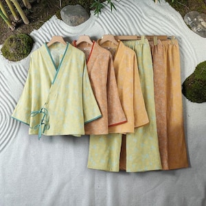 May include: A collection of wrap-style tops and wide-leg trousers in shades of pale yellow, orange, and mustard. Each garment features a subtle, repeating floral pattern. The tops have three-quarter sleeves and tie closures with contrasting trim.