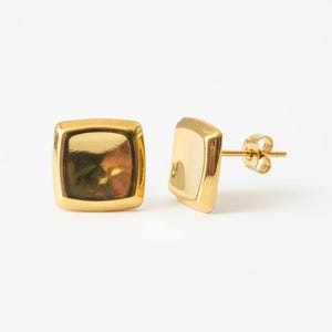 May include: A pair of gold-colored square stud earrings. The earrings have a polished, reflective surface and a post backing. The earrings are displayed on a white background.
