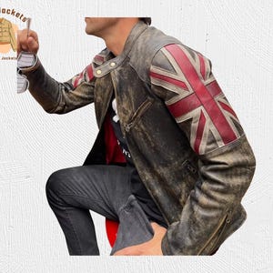May include: A distressed brown leather jacket with a Union Jack flag design on the right shoulder. The jacket has a zipper closure, multiple pockets, and a worn appearance. The Kraft Jackets logo is in the upper left corner.