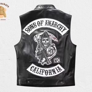 May include: Black leather vest with white patches featuring the text "SONS OF ANARCHY" and "CALIFORNIA". A skull graphic with a scythe and rifle is centered on the back. The vest has a classic biker style.
