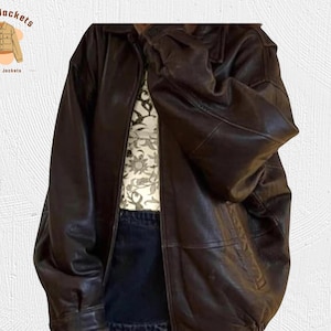 May include: A dark brown leather jacket with a collared neckline and a zipper closure. The jacket has a relaxed fit and appears to be worn over a patterned shirt and denim. The logo "Kraft Jackets Leather Jackets" is in the upper left corner.