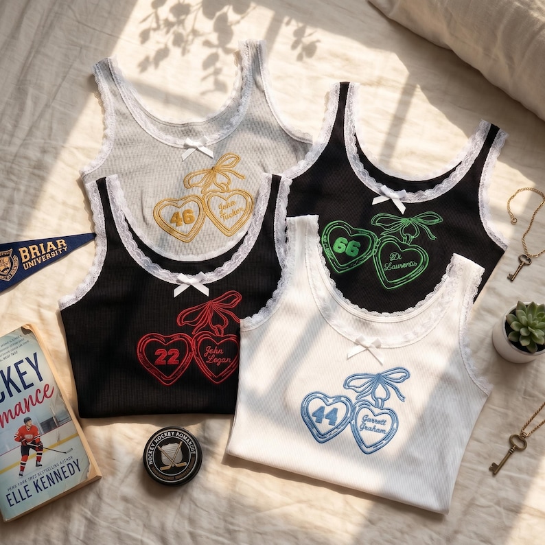May include: Four ribbed tank tops with white lace trim and a small centre bow. Each features an embroidered design of two hearts tied with a bow, containing a number and a name: 46 John Tucker, 66 D. Laurentis, 22 John Logan, and 44 Garrett Graham.