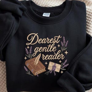 May include: Black sweatshirt featuring gold embroidered text reading "Dearest gentle reader". The design includes a book, quill, and envelope with lavender sprigs. A cosy, literary-themed garment.