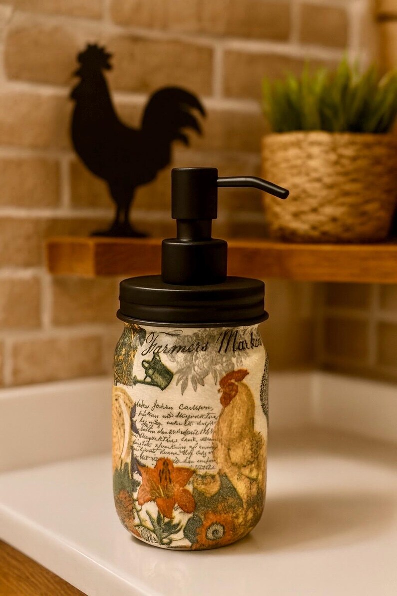 May include: A glass soap dispenser with a matte black pump and lid. The jar features a Farmers Market label, a rooster illustration, floral motifs, and cursive script text. The design includes warm tones of orange, yellow, and green on a light background.
