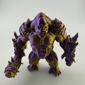 Pode incluir: Uma figura detalhada, impressa em 3D, de uma criatura musculosa semelhante a um macaco com armadura pontiaguda e uma expressão feroz. A figura é principalmente de cor roxa escura com destaques dourados, mostrando texturas e detalhes intrincados.