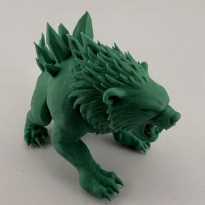 May include: A green, 3D-printed figurine of a snarling, mythical beast. The creature has a lion-like head with sharp teeth and a spiky mane and back. Its paws are extended, and it appears to be in a predatory stance. The figurine is a solid, detailed sculpture.