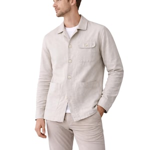 Könnte beinhalten: Hellbeige Leinenjacke mit Knopfleiste, zwei Vordertaschen und einer Brusttasche. Die Jacke hat lange Ärmel und einen Kragen. Das Model trägt ein weißes T-Shirt und eine beige Hose.