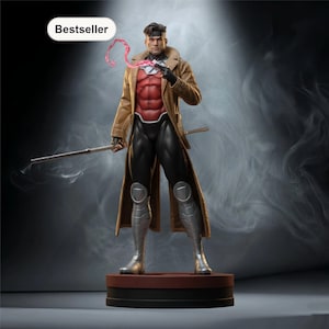 May include: A detailed figurine of the Marvel Comics character Gambit. He is depicted in a brown trench coat, red and black suit, and silver boots. He holds a staff and has a pink energy effect emanating from his hand. The base is brown with a black border. The word "Bestseller" is in a white oval.