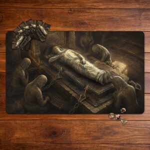 May include: A rectangular playmat featuring a dark, detailed illustration of a figure wrapped in burial cloth lying on a stone sarcophagus, surrounded by hooded, kneeling figures in a dim chamber, with small game cards and dice placed nearby.