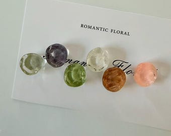 May include: A collection of six colorful, translucent, round beads in shades of green, purple, clear, brown, and pink. The beads are arranged on a white card with the text "ROMANTIC FLORAL".