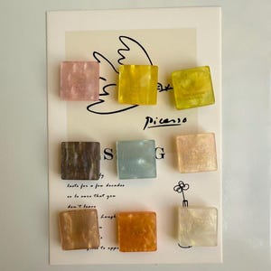 May include: Nine square-shaped decorative magnets in various colors, including pink, yellow, brown, and orange. Each magnet has a slightly translucent appearance and features the text "CREATION FRANCE". The magnets are arranged on a card with a Picasso-style drawing.