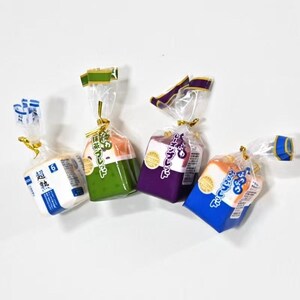May include: Four square-shaped bread loaves in clear plastic packaging with gold ties. The loaves are white, green, purple, and orange, each featuring Japanese text labels including '超熟' on the white loaf and various brand markings on the others.