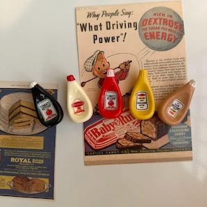 Peut inclure: Des aimants en forme de condiments de style vintage, dont du ketchup, de la mayonnaise et de la moutarde. Les aimants sont disposés près d'une publicité rétro avec le texte "What Driving Power!" et "Baby Ruth".