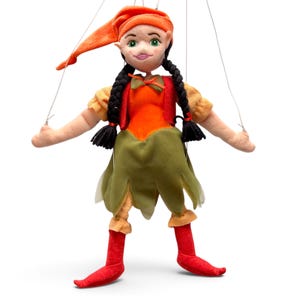 Puede incluir: Una marioneta de peluche que representa un personaje con cabello negro trenzado, ojos verdes y un sombrero naranja puntiagudo. La marioneta viste un corpiño naranja, una falda verde con bordes dentados, mangas color canela y botas rojas puntiagudas.