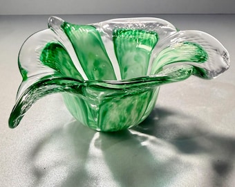 May include: A clear glass bowl with a green and white marbled design. The bowl has a flower-like shape with curved, petal-like edges. The green color is swirled throughout the glass, creating a unique and artistic look. The bowl is likely used for decorative purposes.