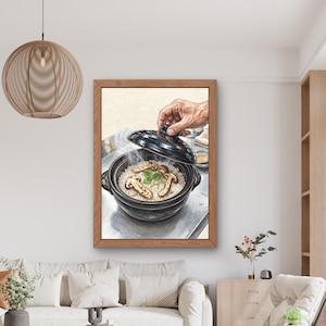 Puede incluir: Una impresión de arte mural enmarcada que muestra una olla de cerámica negra tipo donabe llena de arroz blanco cocido y champiñones marrones en rodajas. Una mano levanta la tapa negra, revelando vapor saliendo del plato caliente.