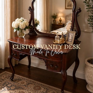 Op de afbeelding: Een op maat gemaakte kaptafel van donker hout met een grote ovale spiegel. De bureau heeft lades en sierlijke details. De tekst "CUSTOM VANITY DESK Made To Order" staat op de voorkant. Een vaas met witte bloemen en decoratieve flessen staan op het bureau.