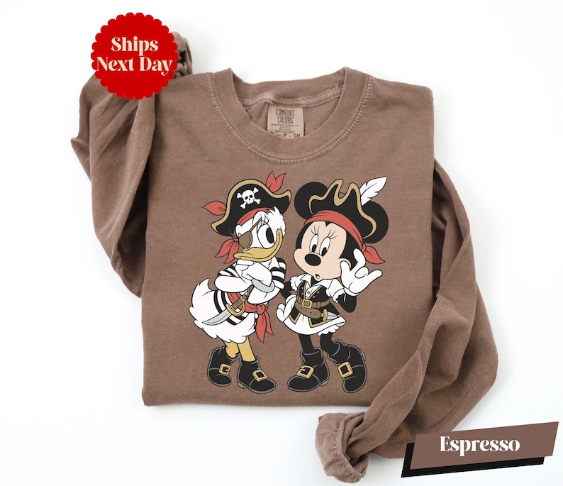 A brown t-shirt with a cartoon image of Minnie Mouse and Donald Duck dressed as pirates, along with a red "Ships Next Day" sticker.