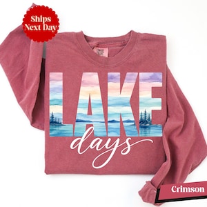 A pink long-sleeved shirt with the word "LAKES" printed on it, along with a scenic landscape of a lake and mountains.