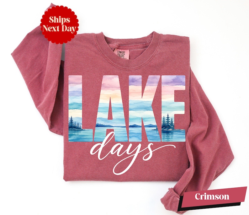 A pink long-sleeved shirt with the word "LAKES" printed on it, along with a scenic landscape of a lake and mountains.