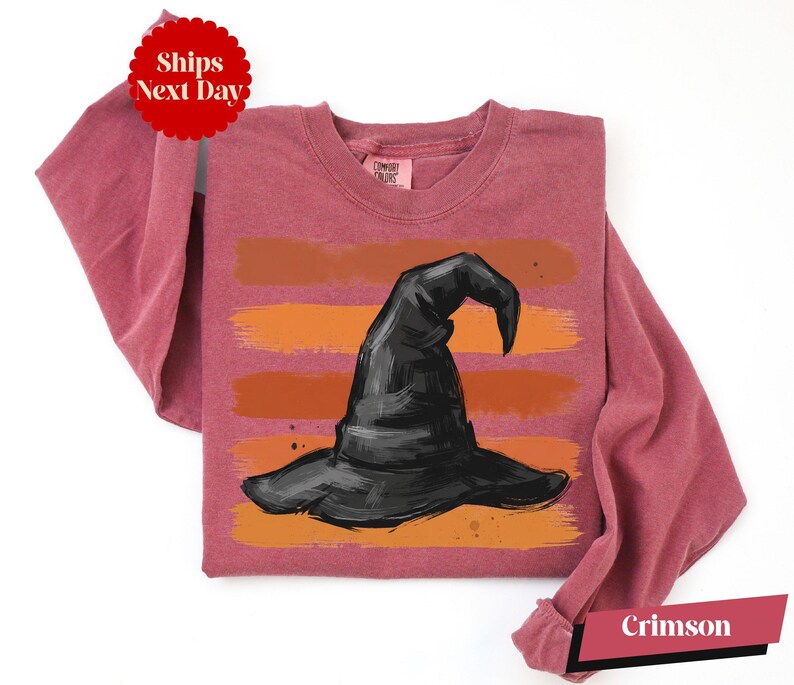 A pink long-sleeved t-shirt with a graphic of a witch's hat printed on it.
